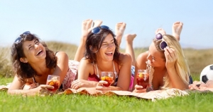 A group of friends lying on a blanket outside and enjoying a drink together