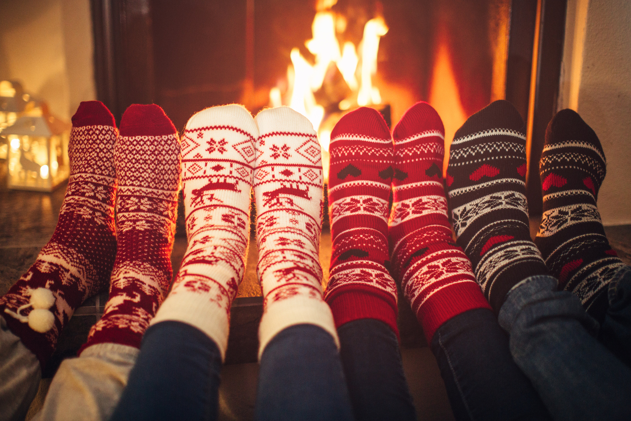 Feet in Christmas socks near fireplace. Four pair of feet warming up. Friends at cozy winter vacation.
